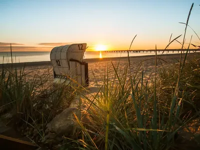 Wundervoller Abend am Strand in Scharbeutz mit Sonnenuntergang, einem Strandkorb und einer Seebrücke im seichten Ostsee-Wasser