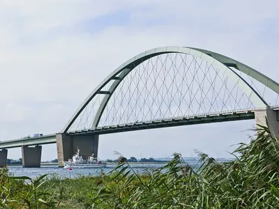 Die Fehmarnsundbrücke in Nahaufnahme aus dem Schilf heraus fotografiert mit einem kreuzenden Schiff