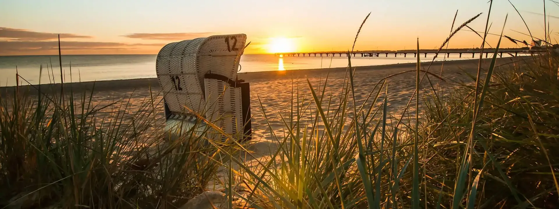 Wundervoller Abend am Strand mit Sonnenuntergang, einem Strandkorb und einer Seebrücke im seichten Ostsee-Wasser